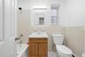 Bathroom with a wood-finish vanity, integrated sink, tiled walls, and a white toilet