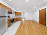 Open-concept living space featuring wood-finish flooring, recessed lighting, wood cabinetry, stainless steel appliances, and white tile flooring in th