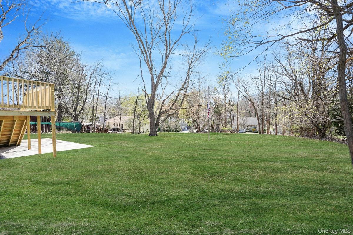 View of grassy yard featuring a wooden deck, stairs, and a patio