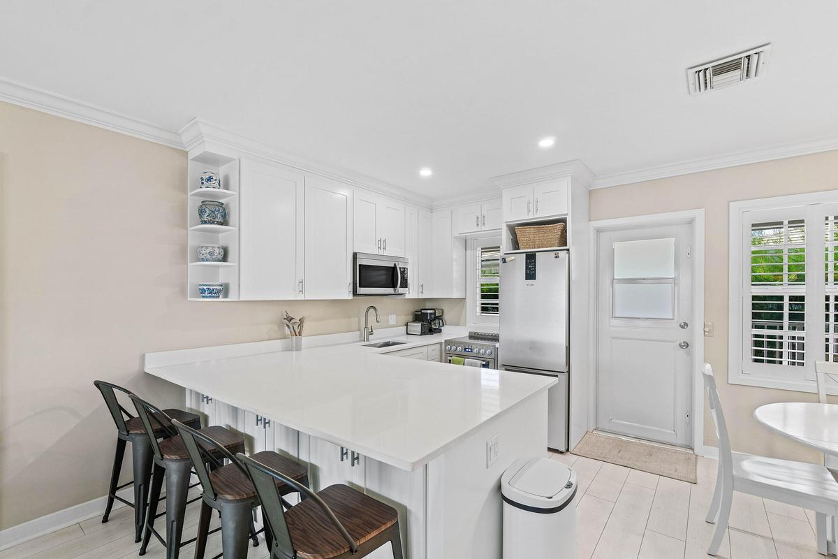 Bright kitchen featuring white cabinetry, stainless steel appliances, corner shelving, and a large breakfast bar with solid surface countertops