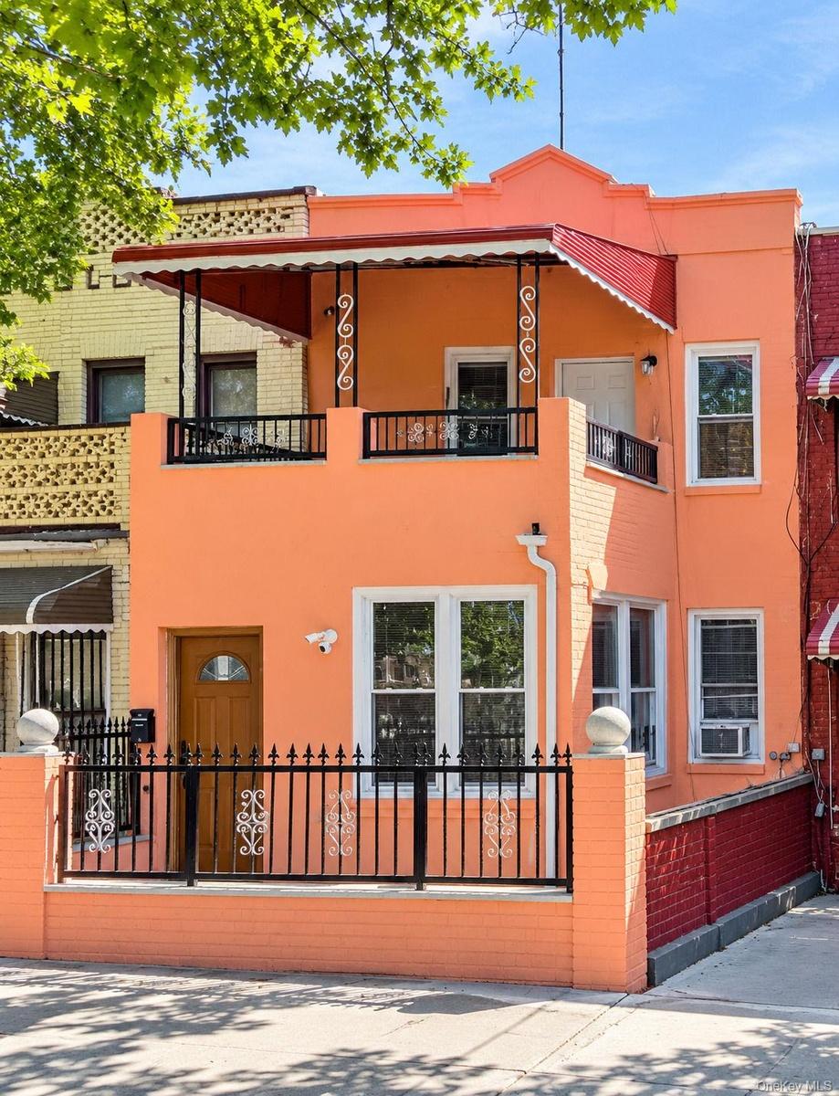 Two-story residential facade with an orange exterior, featuring a second-level balcony with black wrought iron railing and an awning