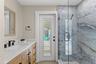 Updated bath features a modern vanity, quartz-style countertop, black fixtures, and a striking glass-enclosed tiled shower.