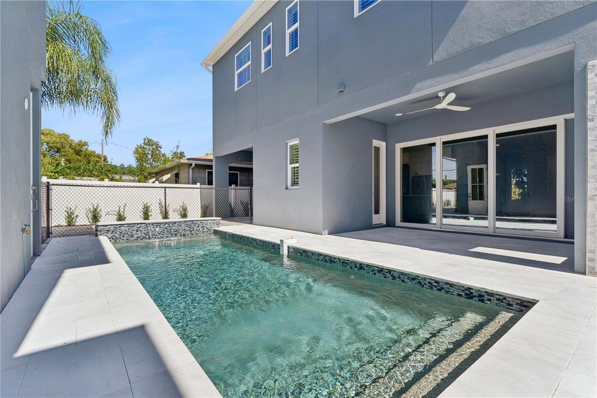 The pool sits beside a paved deck and covered rear patio, creating an inviting outdoor setting.