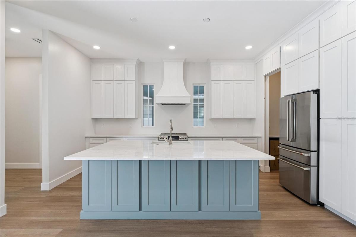 Main kitchen at 3456 Fairway Ln with a blue island, white counters, range hood, and stainless steel appliances.