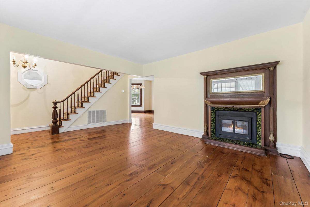 Hardwood flooring throughout, featuring a detailed wooden staircase and an ornate fireplace with an intricate surround