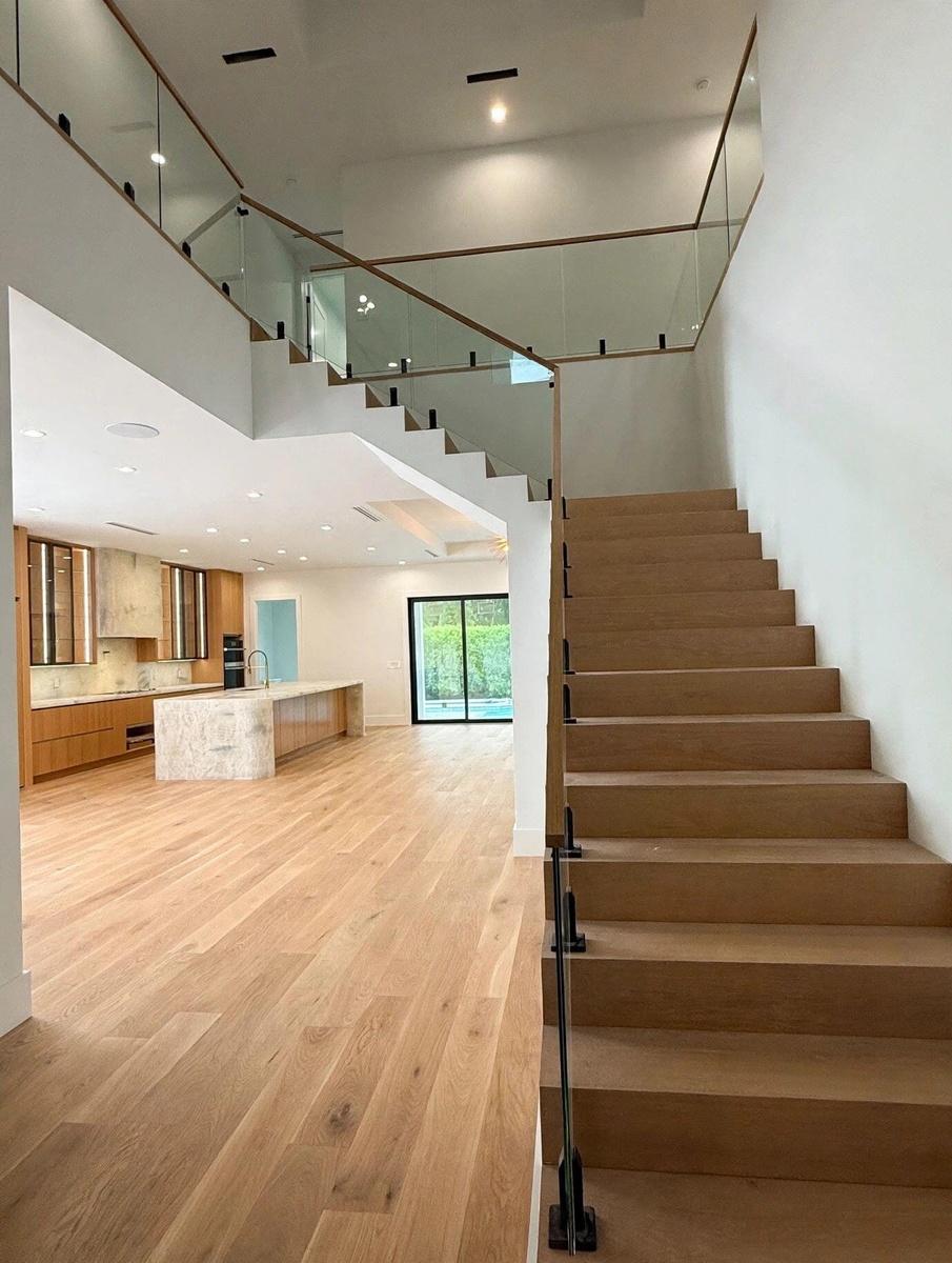 Floating wood staircase with glass railing and wood handrail, hardwood flooring, recessed lighting, and a kitchen featuring a stone-clad island