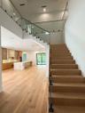 Floating wood staircase with glass railing and wood handrail, hardwood flooring, recessed lighting, and a kitchen featuring a stone-clad island