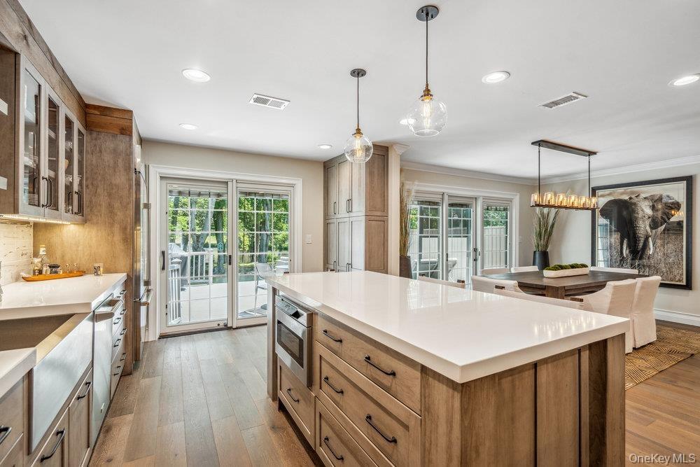 Gourmet kitchen featuring wood-finish flooring, a center island with integrated microwave, white countertops, and glass-paneled upper cabinetry