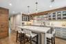 Kitchen featuring a large island with white countertops, wood-finish flooring, exposed wood beam accents, modern pendant lighting, and glass-front upp