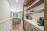 Built-in beverage station featuring open shelving, white countertop, and light wood-finish cabinetry