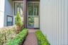 Brick paver pathway with manicured landscaping, vertical panel siding, and a paneled entry door