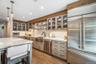Stainless steel appliances, wood-finish flooring, white countertops, textured backsplash, and glass-front cabinetry