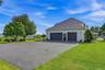 Three-car garage with black doors, paved driveway, expansive green lawn, mature trees, and a distant mountain backdrop
