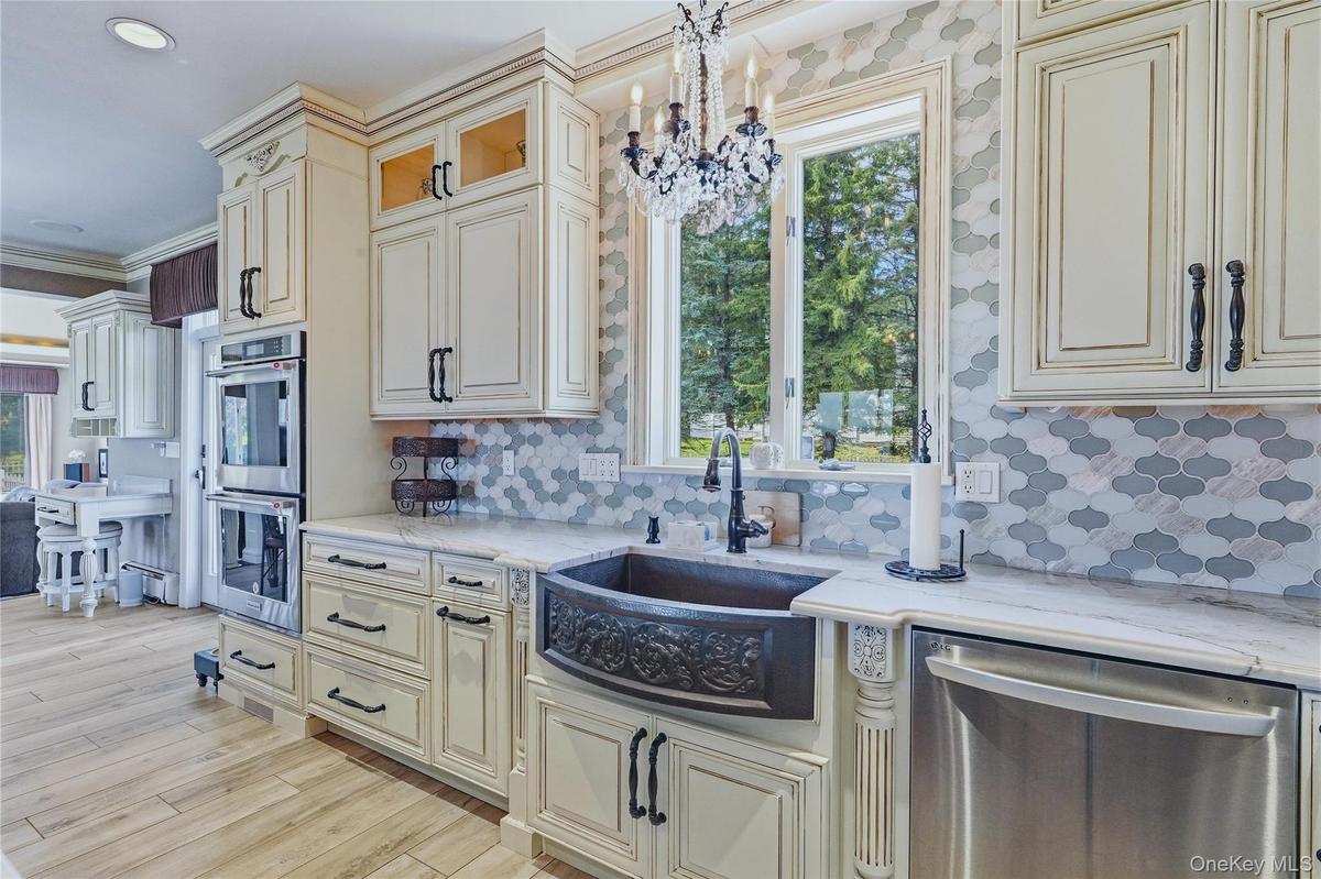 White cabinetry with dark hardware, a decorative marble backsplash, stainless steel appliances, a black farmhouse-style sink, quartzite counter tops