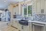 White cabinetry with dark hardware, a decorative marble backsplash, stainless steel appliances, a black farmhouse-style sink, quartzite counter tops