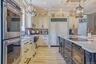 Gourmet kitchen with double wall ovens, integrated refrigerator, custom cabinetry, large kitchen island with cooktop, quartzite counter tops, and wood
