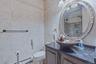 Custom vanity with a dark granite countertop and vessel sink, detailed ornate mirror, and tiled walls with decorative trim
