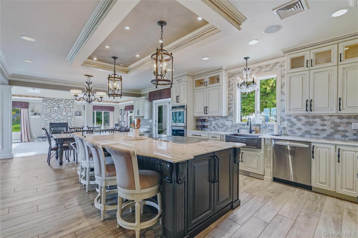 Gourmet kitchen featuring a large central island with seating, white shaker-style cabinetry, stainless steel appliances, and wood-look flooring
