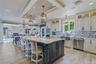 Gourmet kitchen featuring a large central island with seating, white shaker-style cabinetry, stainless steel appliances, and wood-look flooring