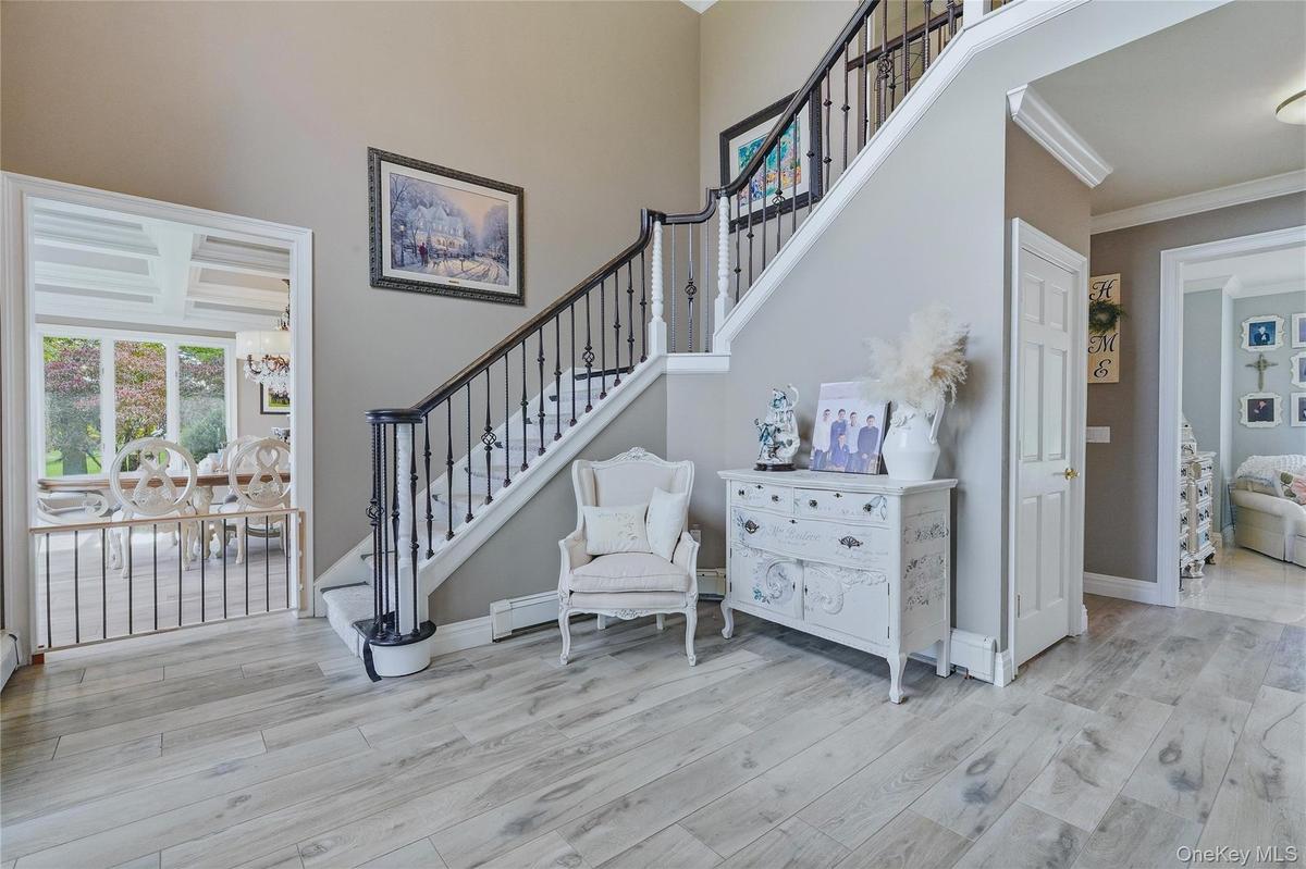 Two-story foyer with wood-look flooring, wrought iron staircase, crown molding, and an arched doorway