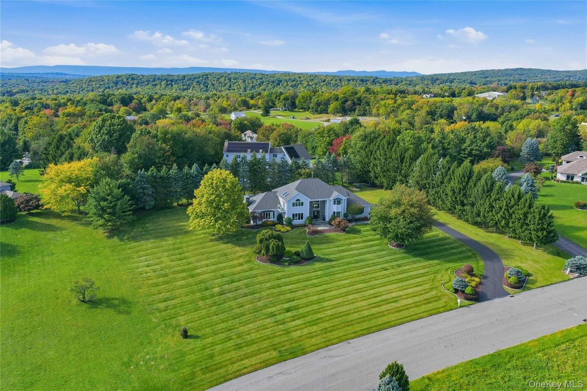 Expansive landscaped grounds with a curved asphalt driveway, mature trees, and a two-story residence featuring a portico entry