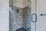 Glass-enclosed shower with a river rock floor, tiled walls, and a built-in shower niche
