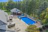 Expansive paver patio featuring a built-in outdoor kitchen, two swimming pools, and a pool house with covered outdoor space