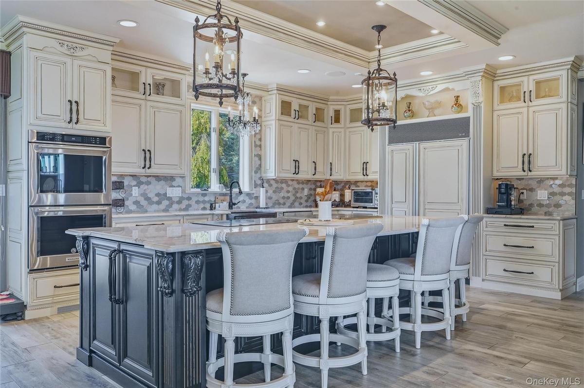 Gourmet kitchen featuring a large central island with seating, stainless steel built-in double ovens, extensive cabinetry, and a patterned marble back