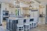 Gourmet kitchen featuring a large central island with seating, stainless steel built-in double ovens, extensive cabinetry, and a patterned marble back