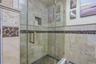Glass-enclosed shower featuring natural stone-finish wall tile, a decorative mosaic tile band, a recessed shower niche, and a river rock-finish shower
