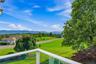 Balcony with glass railing, overlooking expansive landscape featuring rolling green hills, distant mountains, established trees, Hudson River views