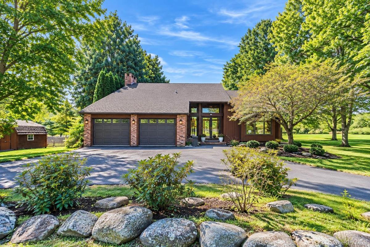 Property exterior featuring a multi-car garage, brick facade accents, a prominent front entrance with transom windows, and mature trees