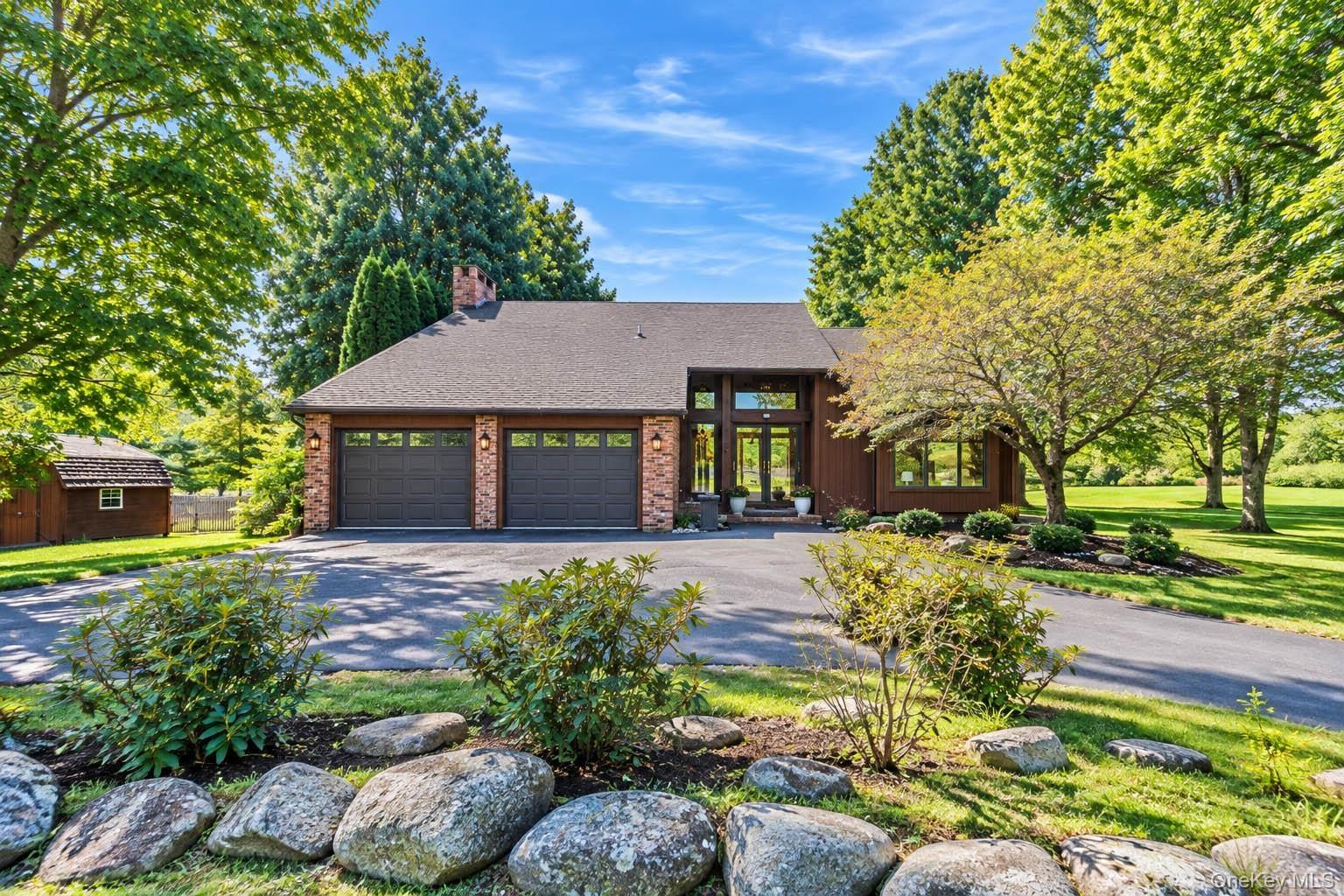 Property exterior featuring a multi-car garage, brick facade accents, a prominent front entrance with transom windows, and mature trees