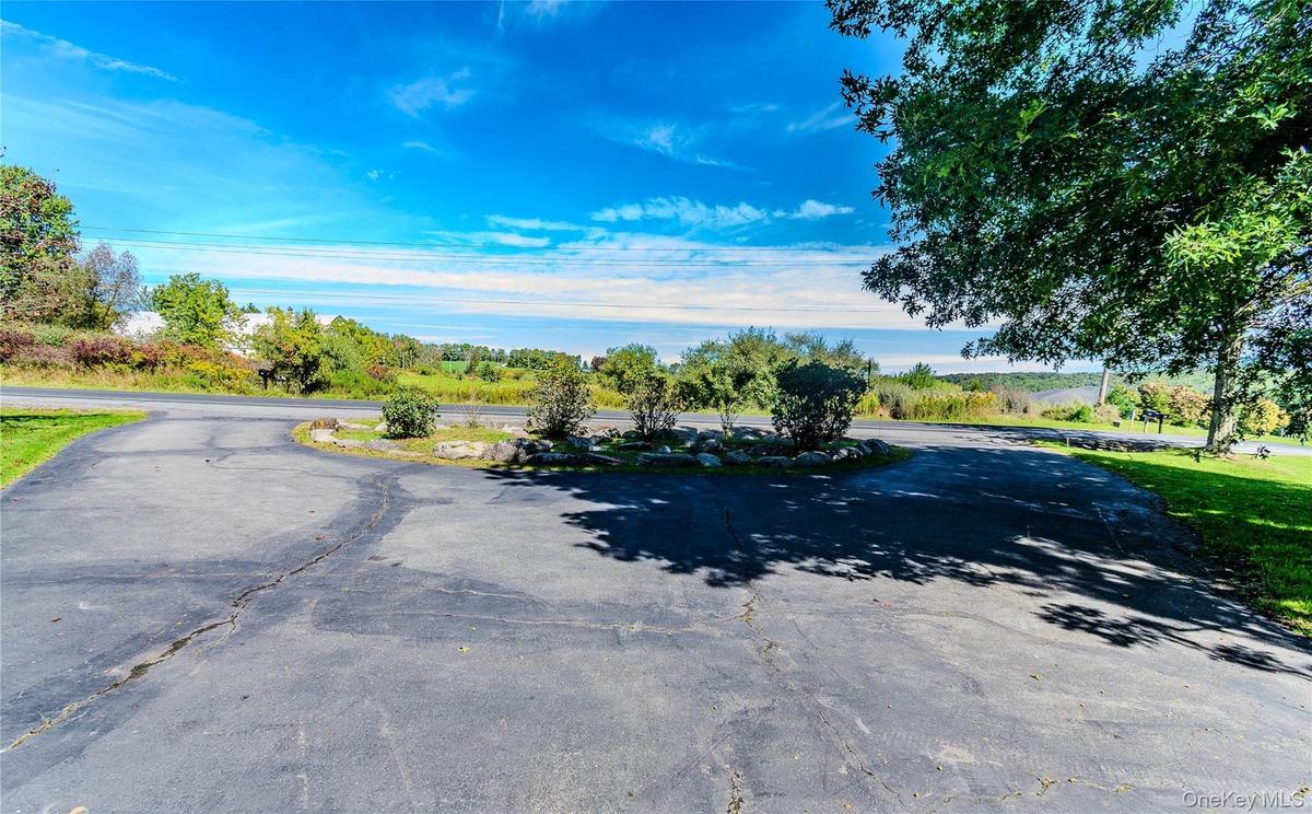 Asphalt driveway with a circular turnaround, surrounded by mature trees and landscaping