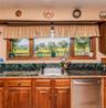Wood-finish cabinetry, stainless steel sink, tile backsplash, and wood-framed windows