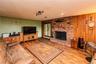 Wood-finish flooring throughout, featuring a brick fireplace with a stone hearth, wood paneling, and a large window