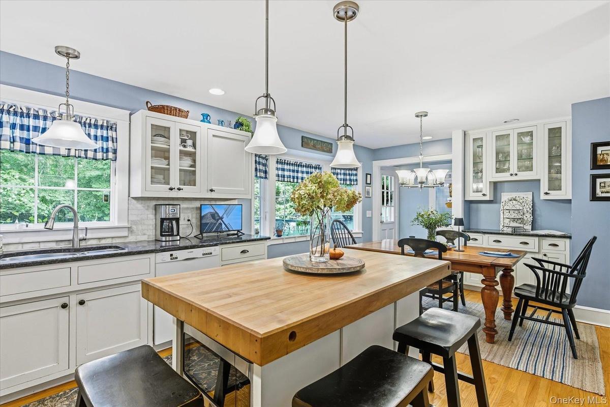 Updated Kitchen featuring a butcher block island, white cabinetry with glass-front uppers, stainless steel sink, and wood-finish flooring
