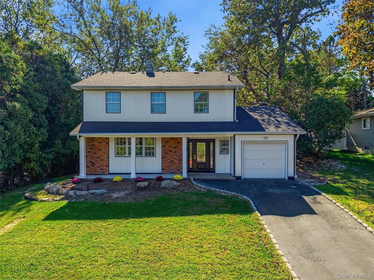 Two-story exterior with white siding and brick accents, featuring a front porch with white columns, an attached single-car garage, and a paved drivewa