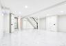 Spacious lower-level area featuring white porcelain tile flooring, recessed lighting, and a white painted staircase with a black handrail