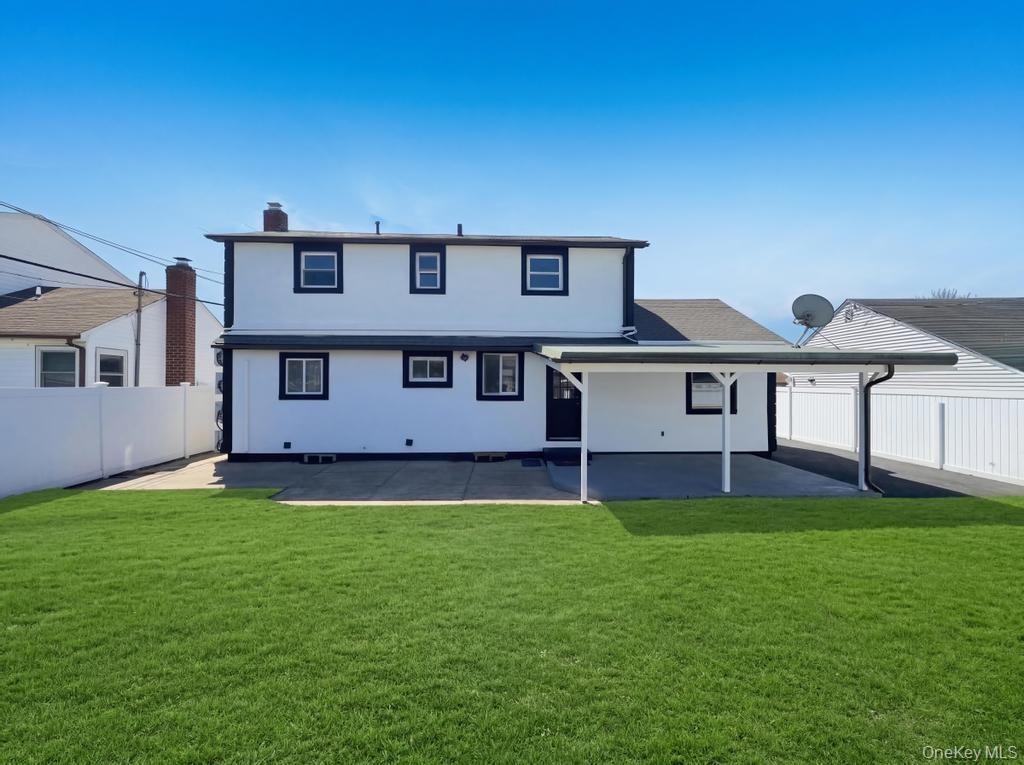 Expansive green lawn with a white two-story exterior featuring dark trim, a covered patio, and a privacy fence