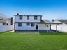 Expansive green lawn with a white two-story exterior featuring dark trim, a covered patio, and a privacy fence