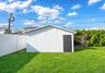 White corrugated metal shed with a dark panel door, set within a vibrant green lawn
