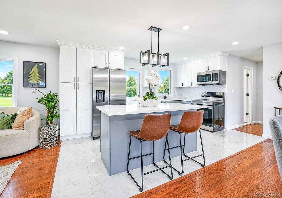 Modern kitchen featuring a central island with a light countertop, white shaker cabinetry, stainless steel appliances, and a mosaic tile backsplash
