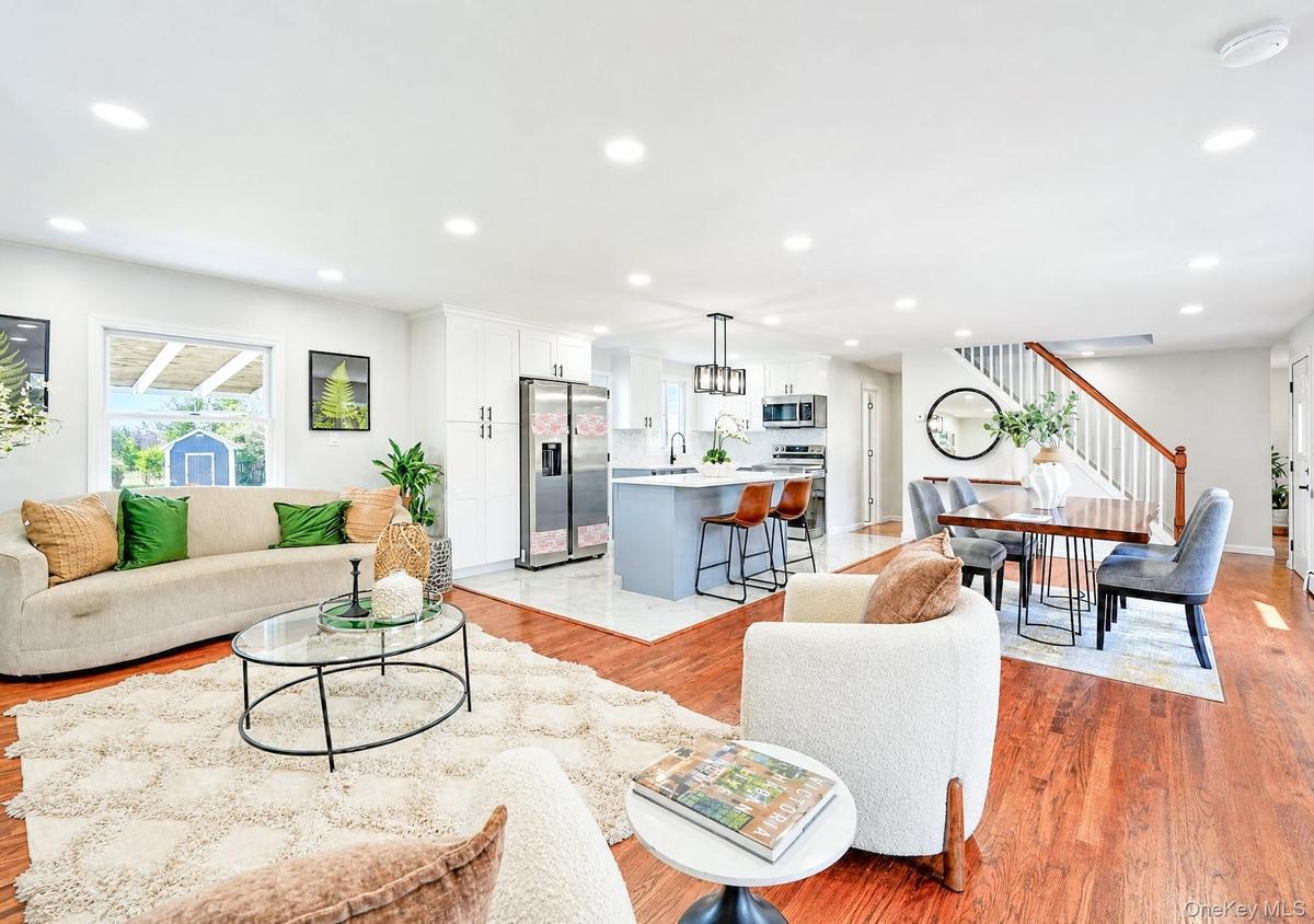 Open-concept living space featuring hardwood flooring, recessed lighting, a modern kitchen island with seating, white shaker cabinetry, and stainless 