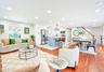 Open-concept living space featuring hardwood flooring, recessed lighting, a modern kitchen island with seating, white shaker cabinetry, and stainless 