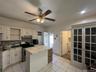 White tile flooring, white cabinetry, stainless steel range with overhead microwave, white island with a light-colored countertop, and a built-in stor