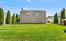 Expansive green lawn with mature evergreen trees and a white privacy fence