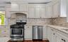 Cream-painted cabinetry, stone backsplash, stainless steel appliances, granite countertops, and wood-finish flooring