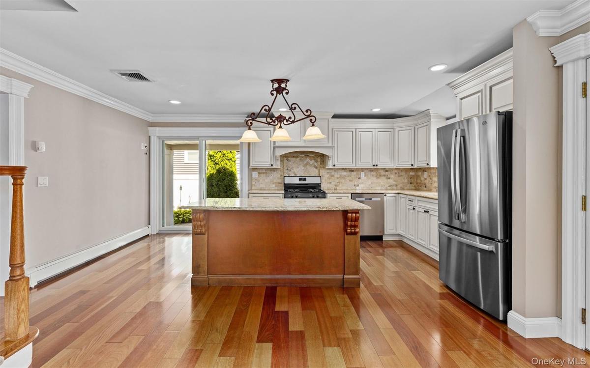 Hardwood flooring throughout, white cabinetry with crown molding, stainless steel appliances, a kitchen island with a stone countertop, and glass slid