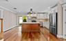 Hardwood flooring throughout, white cabinetry with crown molding, stainless steel appliances, a kitchen island with a stone countertop, and glass slid